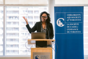 Woman speaking at a podium with Agency banner in background