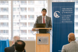 Man providing address at podium with Agency banner in background.